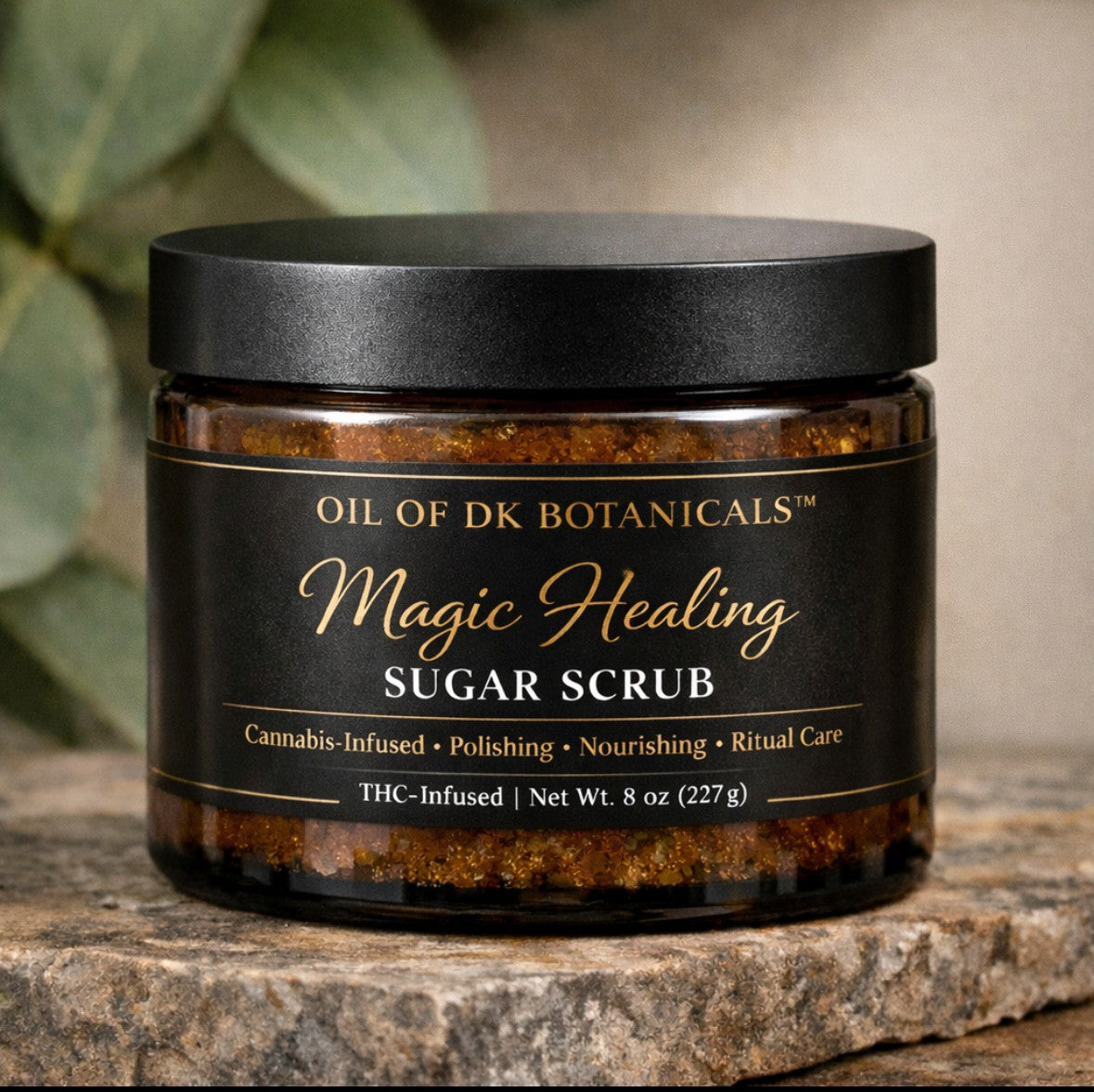Jar of Oil of DK Botanicals Magic Healing Sugar Scrub on a wooden surface with green leaves in the background.